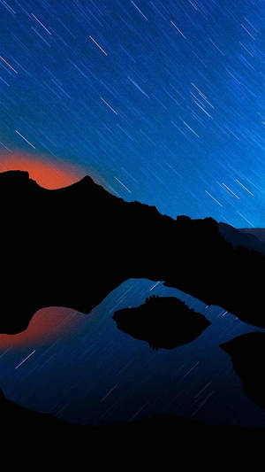 剪影般的山脈和湖泊，在星空下帶有星軌。
