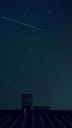一顆流星劃過屋頂和煙囪上方的繁星夜空。
