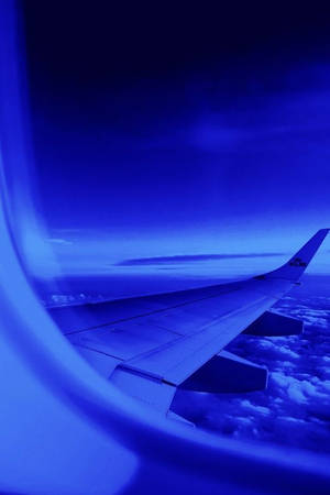 暮色中從窗戶看到雲層上方的飛機機翼。