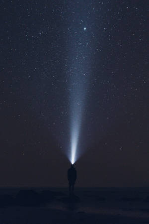 人站在岩石上將手電筒照向星空