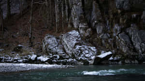 一條積雪的河流流過岩石河岸和光禿禿的樹木，冬季景象。