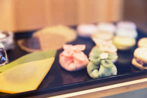 色彩繽紛的日本麻糬糰子排列在深色托盤上，背景甜點柔和。 — MacBook 壁紙