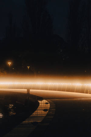 夜晚迷霧中溫暖燈光照亮的彎曲橋樑和濕漉漉的路面
