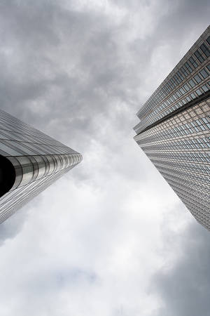 兩座現代玻璃摩天大樓從低角度伸入多雲的天空。 — 天際線 壁紙