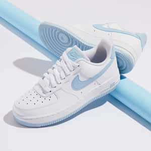 白色Nike Air Force 1運動鞋，帶有淺藍色細節，置於藍色圓柱體和白色表面上。