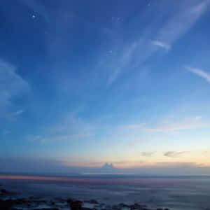 黃昏海洋，平靜的水面和岩石上方有星星和雲彩。 — 藍天 壁紙