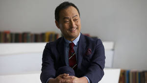 穿西裝的男人在室內書架附近微笑雙手合十。