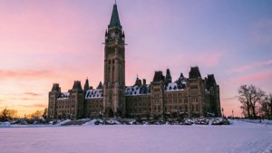 粉紅和紫色日落中白雪覆蓋的議會大樓與鐘樓