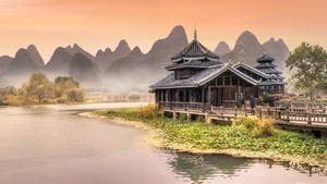河岸上的傳統木造亭子，背景是霧氣瀰漫的山脈