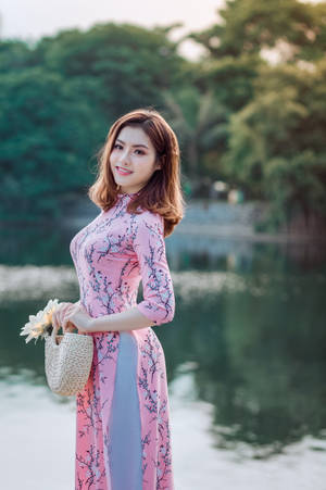 身穿粉紅色奧黛的女性手持竹袋在湖邊