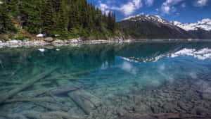 寧靜的山間湖泊，清澈的湖水倒映著積雪的山峰和常綠樹木。
