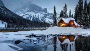 舒適小屋在雪中發光，夜間冰凍湖面反射山景 — 自然 壁紙