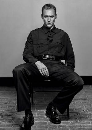 一名身穿深色制服的男人坐在工作室的椅子上，地板是磚的。 — 約翰·卡特 壁紙
