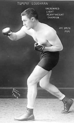 拳擊手 Tommy Loughran 擺出戰鬥姿勢的復古照片，帶有文字疊加。 — 黑白 壁紙