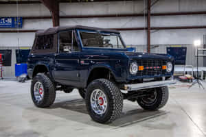 車庫工場中，一輛光澤藍色經典福特Bronco，配備鍍鉻車輪。