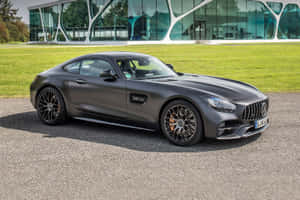 啞光灰色 Mercedes-AMG GT 停泊喺現代玻璃建築前面。