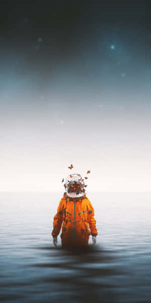 身穿橙色太空衣的太空人，蝴蝶從頭盔飛出，站在星空下的水中。