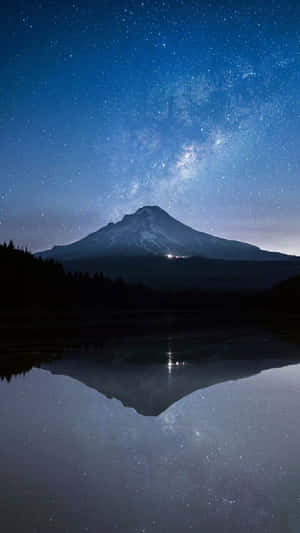 山峰和星空在夜晚平靜的湖面上形成倒影。