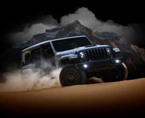 銀色Jeep Rubicon夜間在沙漠沙地上行駛，背景有山脈。
