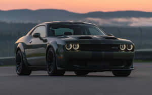 深綠色Dodge Challenger SRT Hellcat在日落時分的賽道上，背後有霧氣繚繞的山脈。