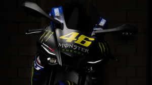 黑色Yamaha賽車電單車，帶有黃色46 Monster Energy標誌，背景為磚牆。