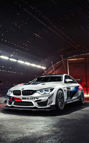 在光線昏暗的車庫中，一輛帶有藍紅塗裝的白色BMW M4 GT4賽車。