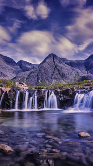 瀑布流過岩石，流入被山環繞的水潭，天空多雲。