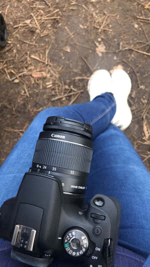 Canon DSLR相機在膝上，配藍色牛仔褲和白色運動鞋，森林地面