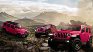 三輛粉紅色Jeep Rubicon SUV在岩石地形上行駛，背景有山脈。