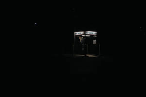 夜晚在黑暗空蕩的停車場中一個亮著的公共電話亭。