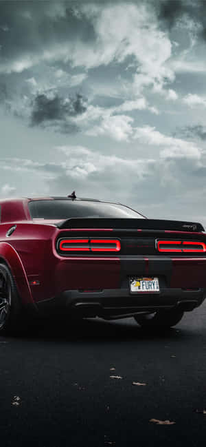 暴風雨天空下，濕路上亮著尾燈的紅色Dodge Challenger Hellcat。 — iPhone 14 Plus 壁紙