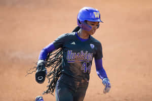 女壘球運動員在泥地球場上奔跑，身穿紫色和黑色 Huskies 球衣。