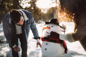 一對情侶在日落時分的雪地森林中堆雪人。 — 美學 壁紙