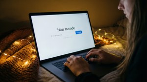在溫暖的串燈下，一個人在筆記型電腦上打字，搜尋查詢為「How to code」。