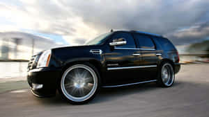 黑色Cadillac Escalade SUV在海濱道路上飛馳，帶有動態模糊效果。