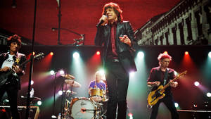 Rolling Stones 在彩色燈光下，手持結他和鼓，現場舞台表演。