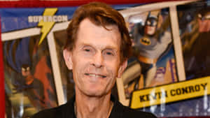 Kevin Conroy 在漫畫展上微笑，身後有蝙蝠俠海報。 — 蝙蝠俠標誌 壁紙