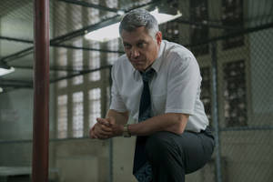 身穿商務服裝的男子在粗糙的工業環境中蹲下。 — Netflix GIF 壁紙