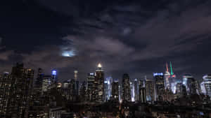 夜間紐約天際線，燈火通明的建築和多雲天空中的明亮月亮。