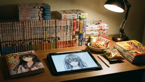 舒適書桌，有漫畫、零食和平板電腦在溫暖燈光下顯示動漫女孩圖畫。