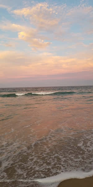 夕陽下的海浪，粉紅色和藍色的天空倒映在水面上。