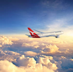 澳洲航空飛機在夕陽下飛越金色雲層。