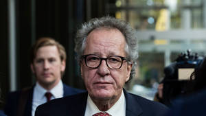 一位身穿西裝、戴眼鏡的嚴肅年長男性被相機包圍。