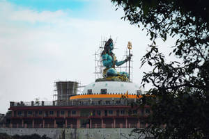 被樹枝環繞的寺廟圓頂上，一座正在建造中的大型藍色濕婆神像。