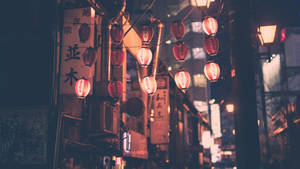 一串發光的紅色燈籠懸掛在夜晚狹窄的日本街道上。 — 唐人街 GIF 壁紙