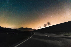 一條黑暗蜿蜒的道路穿過山脈，在星空下閃爍著極光。 — 道路 壁紙