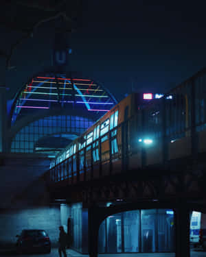 夜間，一列火車經過霓虹燈照亮的車站拱門下方，下方有一個孤獨的身影。