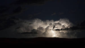 閃電在夜間穿過暴風雲，照亮黑暗的山丘。