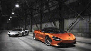 兩輛McLaren超級跑車停放在黑暗的工業倉庫中，頭頂有鋼樑。 — 麥拿侖 GIF 壁紙