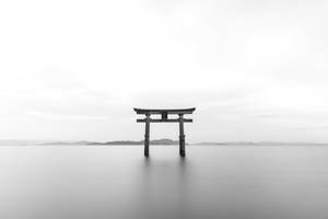 一座傳統的日本鳥居矗立在靜止的水面上，遠方有山丘。 — 日本 壁紙